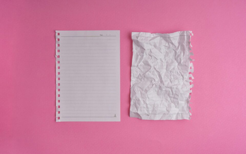 Two sheets of lined paper on a pink background: one is clean and intact, the other is crumpled and torn at the edges. Can be used to note down a line-by-line budget.